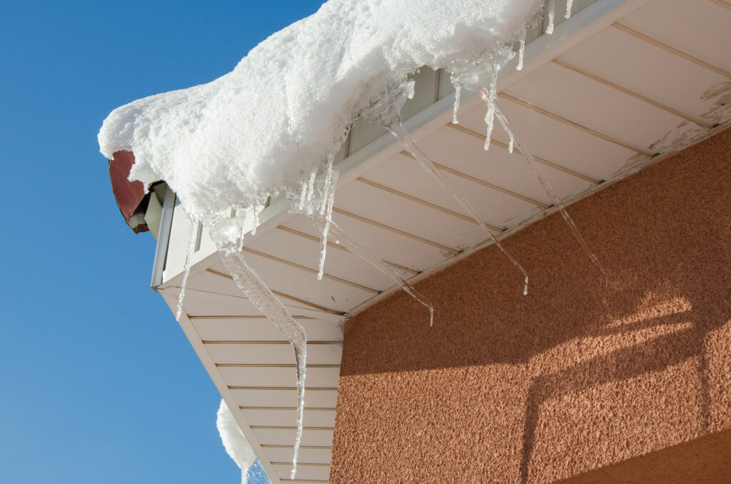 The icicles hanging from the rim of the roof. The spring background of melting ice and snow in the sunny day.